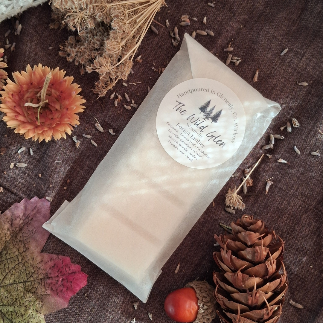Waxmelt in a clear packaging on a wooden surface with dried flowers and a pine cone.