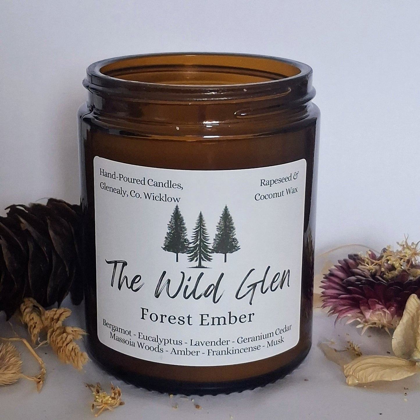 Brown candle jar labeled 'The Wild Glen Forest Ember' with decorative elements on a light background